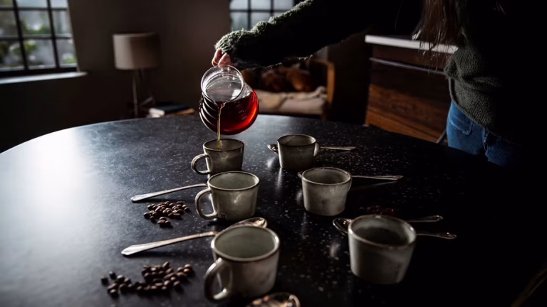 Pouring African single estate coffee from a glass carafe into handmade ceramic cups